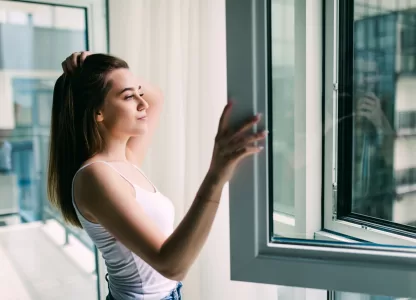 Mulher abrindo janela acústica em apartamento, mostrando como o isolamento ajuda a reduzir o ruído urbano e preservar a saúde.