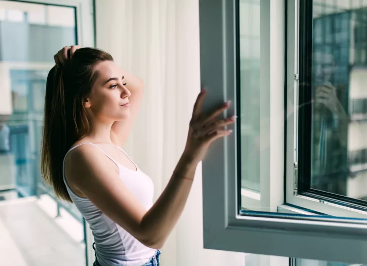 Mulher abrindo janela acústica em apartamento, mostrando como o isolamento ajuda a reduzir o ruído urbano e preservar a saúde.