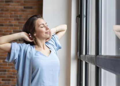 Mulher relaxando próxima a uma janela moderna sob medida em ambiente residencial com parede de tijolos.