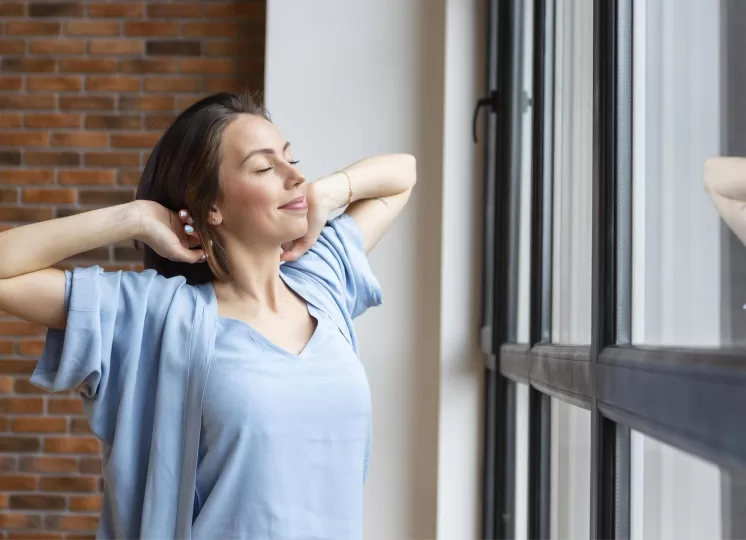 Mulher relaxando próxima a uma janela moderna sob medida em ambiente residencial com parede de tijolos.