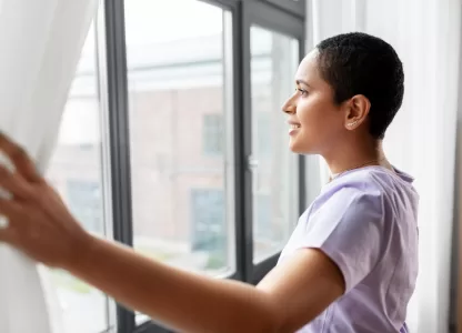 Mulher abrindo cortina diante de uma janela antirruído moderna, aproveitando o silêncio e conforto acústico do ambiente.